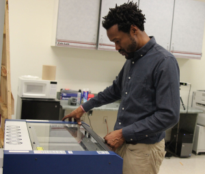 Dr. Eric Saliim working the Epilog Laser, which can cut through plastic, wood, glass and more. Photo by Tia Mitchell/Assistant editor.